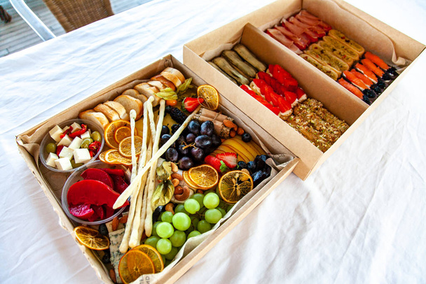 Deliziosi spuntini di vino in una scatola di cartone per un buffet per una festa: formaggi, salumi, salumi, frutta, baguette, Grissini - Foto, immagini