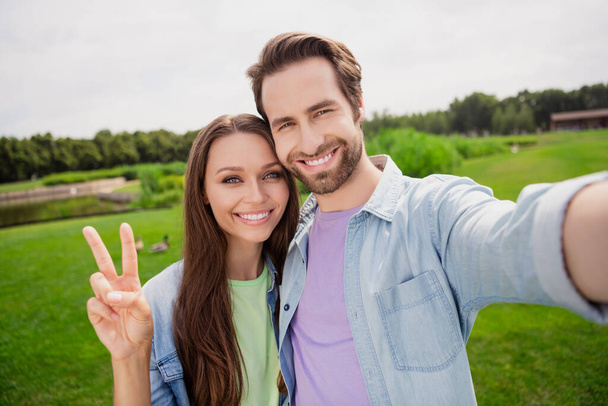 Photo of positive lovely cute married couple take selfie woman showing v-sign relaxing outdoors outside spend free time together - Foto, Imagem