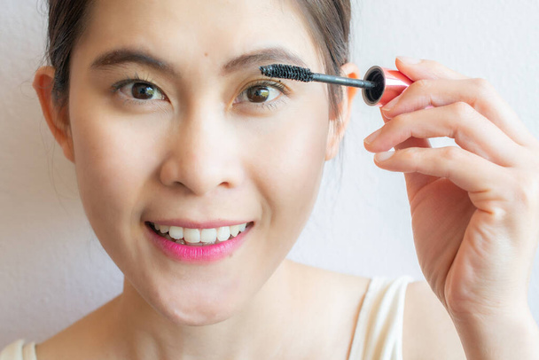 Detailní záběr mladé asijské ženy nanášení černé řasenky na řasy s make-up štětcem. Řasenka je kosmetika běžně používaná ke zvýšení řas. - Fotografie, Obrázek
