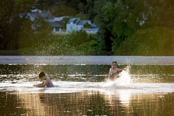Beautiful portrait of children in lake, kids playing in the water on sunset, summertime - Photo, Image