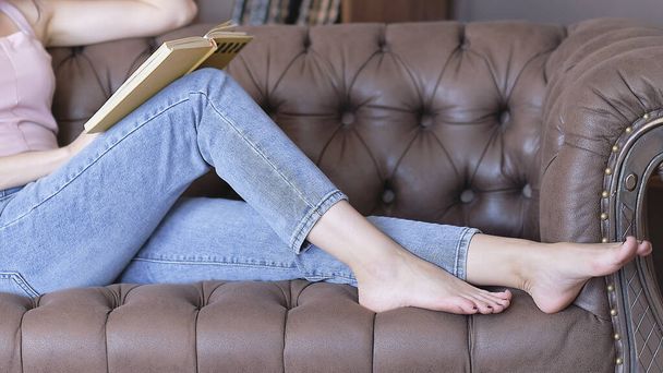 unrecognizable women dressing jeans reading a book sitting on the couch. depression, loneliness concept - Fotó, kép