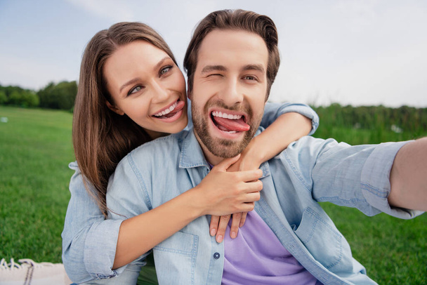 Photo of funky funny smiling couple take selfie fooling around show tongue childish behavior relaxing outdoors outside - Foto, Imagen