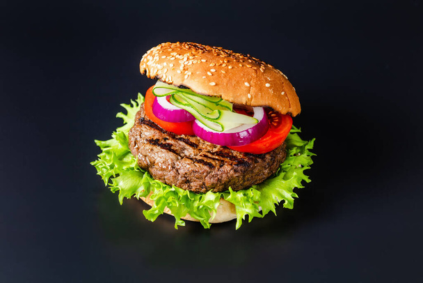 Juicy Grilled Hamburger with Lettuce, Tomato, Red Onion and Cucumber slice on a Bun on a black background - Φωτογραφία, εικόνα