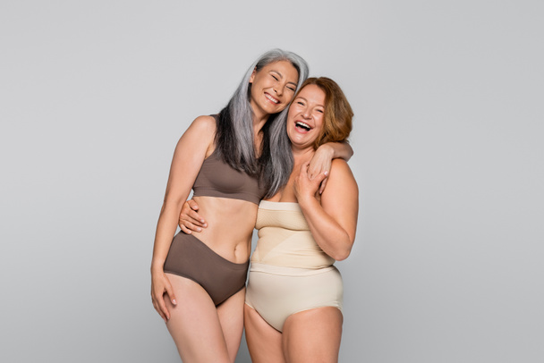 Asian woman in lingerie hugging cheerful friend isolated on grey, body positive concept - Fotografie, Obrázek