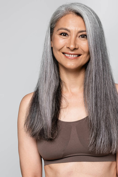 Smiling grey haired woman in bra looking at camera isolated on grey - Fotoğraf, Görsel