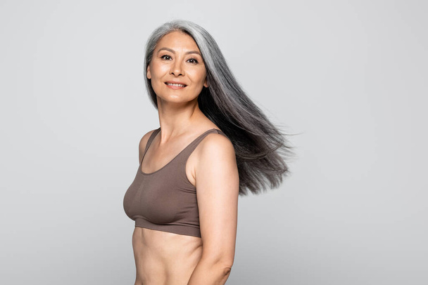 Asian woman in bra smiling at camera isolated on grey, body positive concept - Photo, Image