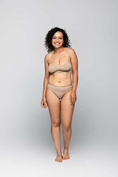 Cheerful african american woman in underwear standing on grey background  - Zdjęcie, obraz