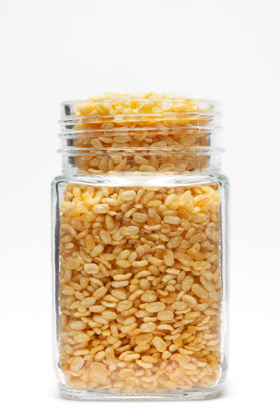 Crunchy Moong Dal in a glass jar, made with roasted Mung bean. Pile of Indian spicy snacks (Namkeen), under backlight, side view, against the white background. - Foto, Imagem