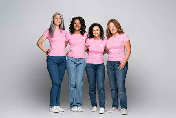 Усміхнені міжрасові жінки зі стрічками усвідомлення раку молочної залози на сірому фоні
  - Фото, зображення