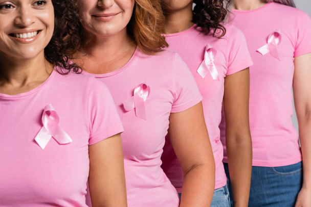 Afroamerikanerin mit rosa Schleife auf T-Shirt lächelt in der Nähe von Freunden isoliert auf grau - Foto, Bild