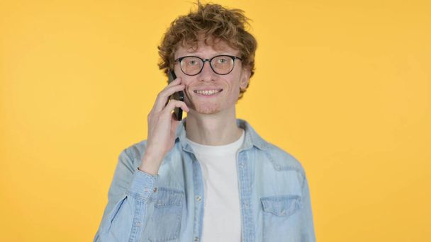 roodharige jongeman praten over de telefoon op gele achtergrond - Foto, afbeelding