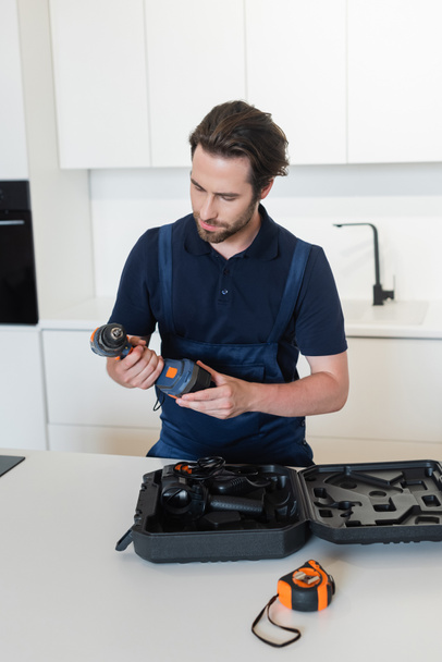 reparador sosteniendo taladro eléctrico cerca de caso en la cocina - Foto, Imagen