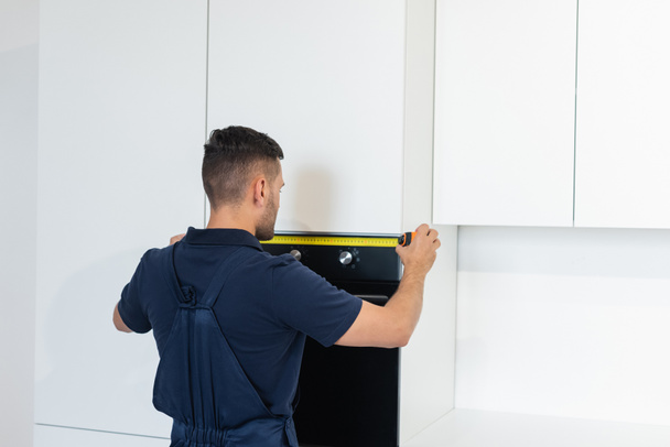 workman measuring electric built-in oven in modern kitchen - Foto, Bild