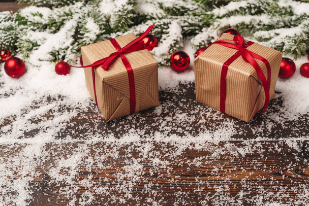Presents on wooden background with fir tree branches and red baubles powdered with snow - Photo, image