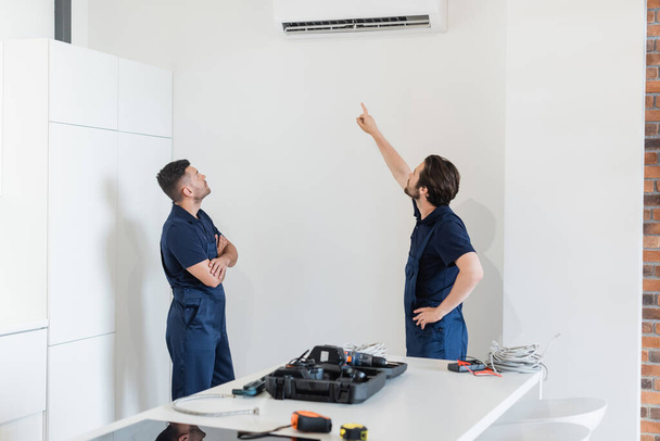 repairman pointing at air conditioner near colleague and tool on kitchen table - Photo, Image