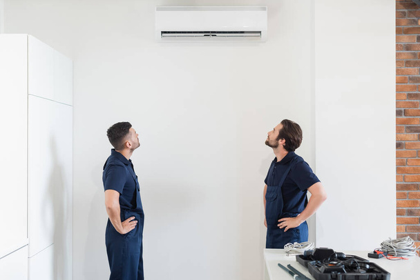 repairmen looking at air conditioner on white wall in kitchen - Photo, Image
