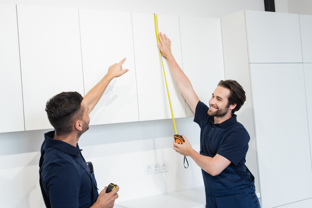 worker pointing with finger near colleague measuring furniture in kitchen - Photo, Image