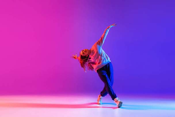 Young beautiful girl, female hip-hop dancer isolated on gradient pink purple neon studio background - Photo, Image
