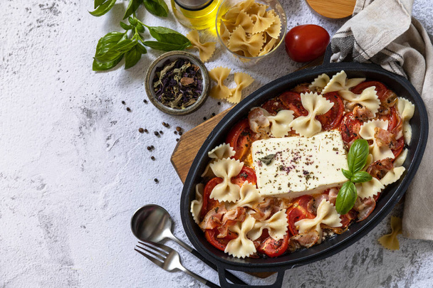 Gebakken feta pasta, of Tiktok pasta op grijze achtergrond. Oven gebakken feta pasta gemaakt van tomaten, feta kaas, knoflook en kruiden. Bovenaanzicht platte achtergrond. Kopieerruimte. - Foto, afbeelding