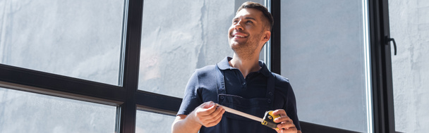 smiling foreman holding measuring tape while standing near windows, banner - Foto, imagen