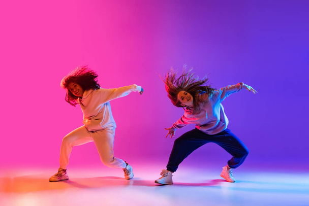 Dwie piękne aktywne dziewczyny tańczące na gradientowym różowym neonie studio tło - Zdjęcie, obraz