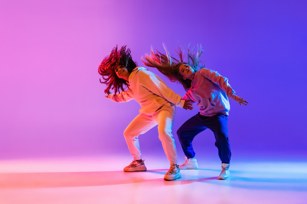 Two beautiful active girls dancing on gradient pink purple neon studio background - Photo, Image