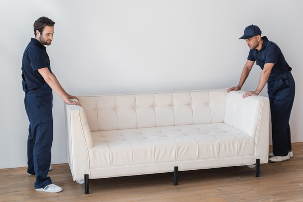 movers in uniform standing near white couch in living room - Photo, Image