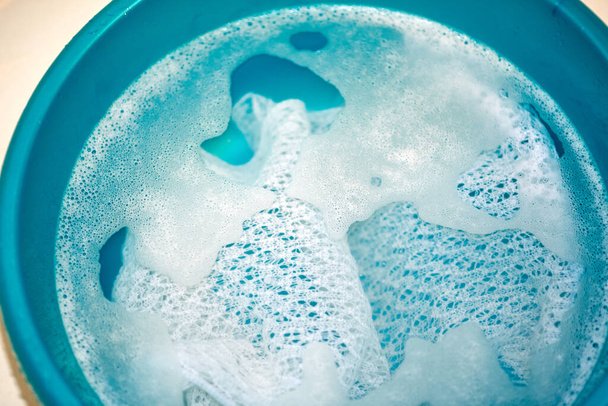 Weißer durchbrochener Strickschal, der in einem grünen Plastikbecken gewaschen wird - Foto, Bild