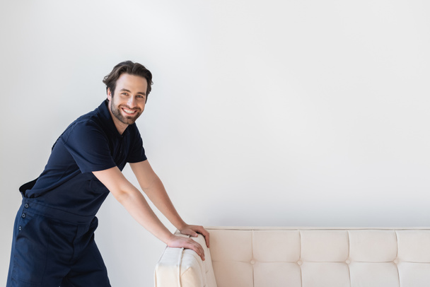 happy mover smiling at camera while standing near white couch - Φωτογραφία, εικόνα
