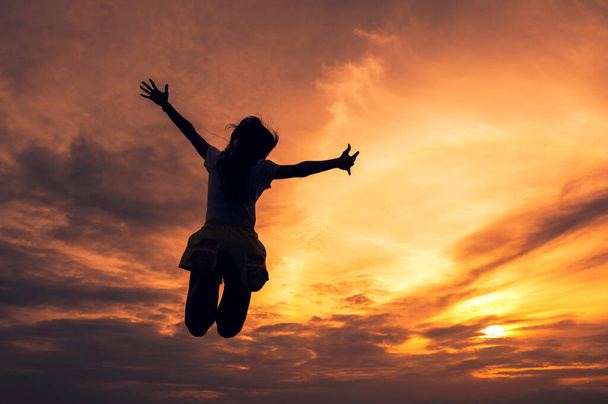 Silhouette giovane donna di successo saltando mani tese nel cielo colorato tramonto - Foto, immagini