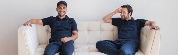 positive Handwerker in Overalls sitzen auf weißer Couch, Banner - Foto, Bild