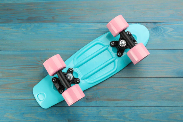 Bright skateboard on turquoise wooden background, top view. Sport equipment - Фото, изображение