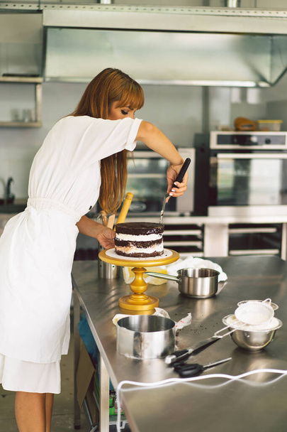 Confectioner girl prépare un gâteau biscuit à la crème blanche et au chocolat. Gâteaux de cuisine. - Photo, image