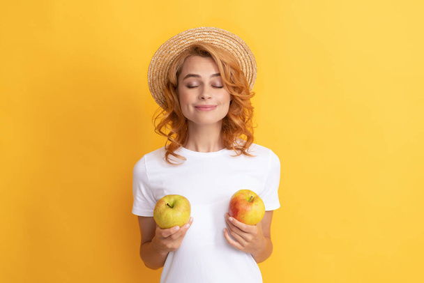 glimlachende roodharige vrouw in stro hoed houden appel, biologisch voedsel - Foto, afbeelding