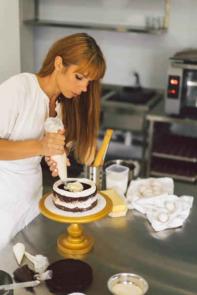Confectioner girl is preparing a cake biscuit with white cream and chocolate. Cooking cakes. - Photo, Image