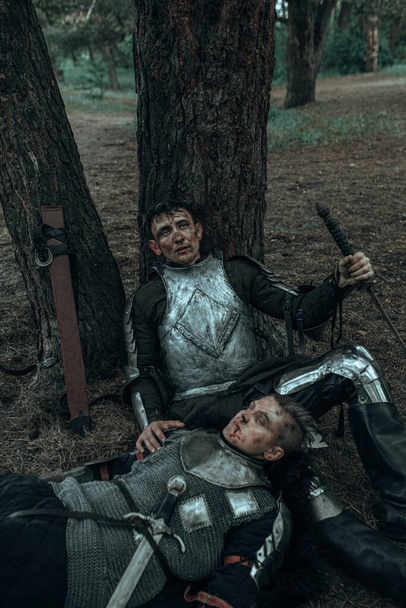 İki yorgun ortaçağ savaşçısı zırhlı şövalyeler ağaçların altında kılıçlarıyla dinleniyorlar.. - Fotoğraf, Görsel
