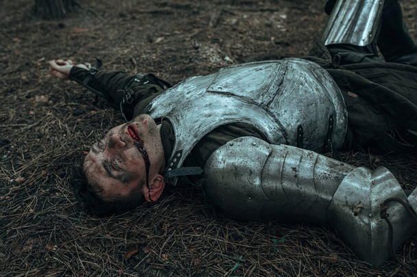 Derrotado en batalla caballero medieval con armadura yace en el campo de batalla entre el bosque. - Foto, imagen