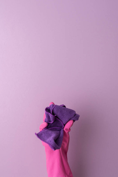 A hand in a pink protective rubber glove holds a microfiber cloth for washing on a purple background - Φωτογραφία, εικόνα