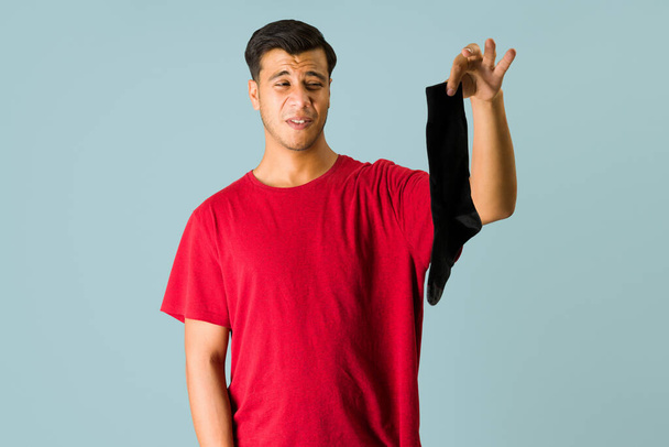 Minun pitää pestä pyykkini. Latino nuori mies poimien likainen sukka ja valmis pesemään vaatteensa  - Valokuva, kuva