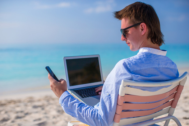 Joven hombre de negocios usando portátil en la playa tropical
 - Foto, Imagen