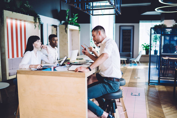 Вид збоку на наміри багатонаціональних офісних працівників у формальному одязі, що розмовляють і жестикулюють, сидячи за столом з документами в сучасному офісі
  - Фото, зображення