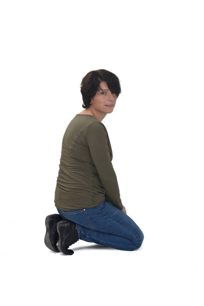 вид сбоку женщины, стоящей на коленях на белом фоне и смотрящей в камеру - Фото, изображение