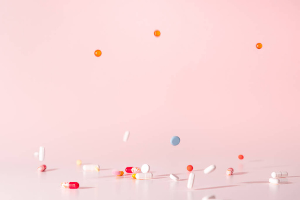 Különböző színes pirulák potyogtak felülről. A gyógyszerek az asztalra ugrottak. Rózsaszín háttér. Szelektív koncentrálás a drogokra. Pilulák mozgásban. Közelkép. - Fotó, kép
