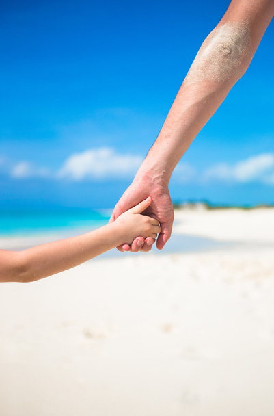 lähikuva isästä ja pienestä lapsesta pitämässä toisiaan kädestä rannalla
 - Valokuva, kuva