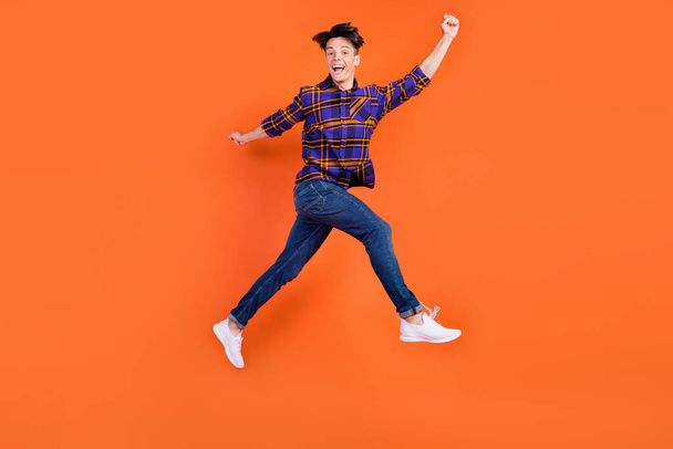 Full length profile photo of young hooray guy jump wear shirt jeans sneakers isolated on orange background - Fotoğraf, Görsel