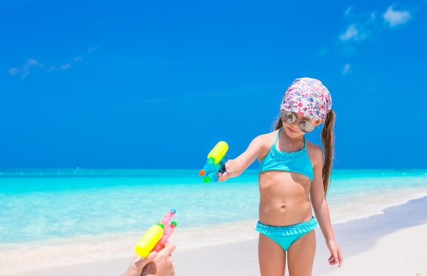 kleines Mädchen spielt mit Wasserpistole am tropischen Strand - Foto, Bild