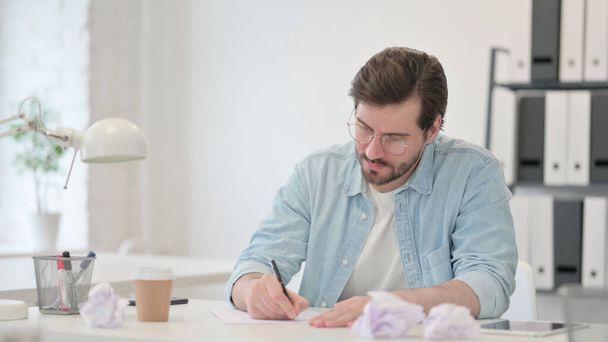 Pessimistischer junger Mann beim Versuch, auf Papier zu schreiben - Foto, Bild