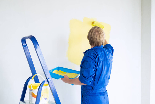 άντρας ζωγραφίζει τοίχο σε κίτρινο χρώμα με ρολό. Σχέδιο ανακαίνισης, επισκευής και ανακαίνισης. - Φωτογραφία, εικόνα