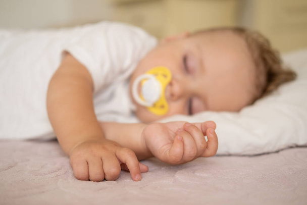 cute baby boy with nipple sleeping on bed at home. selective focus on hands. - Fotografie, Obrázek