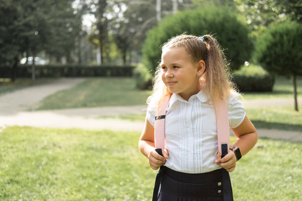gelukkig blond krullend schoolmeisje in school uniform met roze rugzak terug naar school outdoor. - Foto, afbeelding